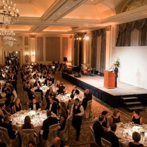 Corporate event in a luxury hotel ballroom with a speaker at a dark wood podium on a raised modular stage with steps